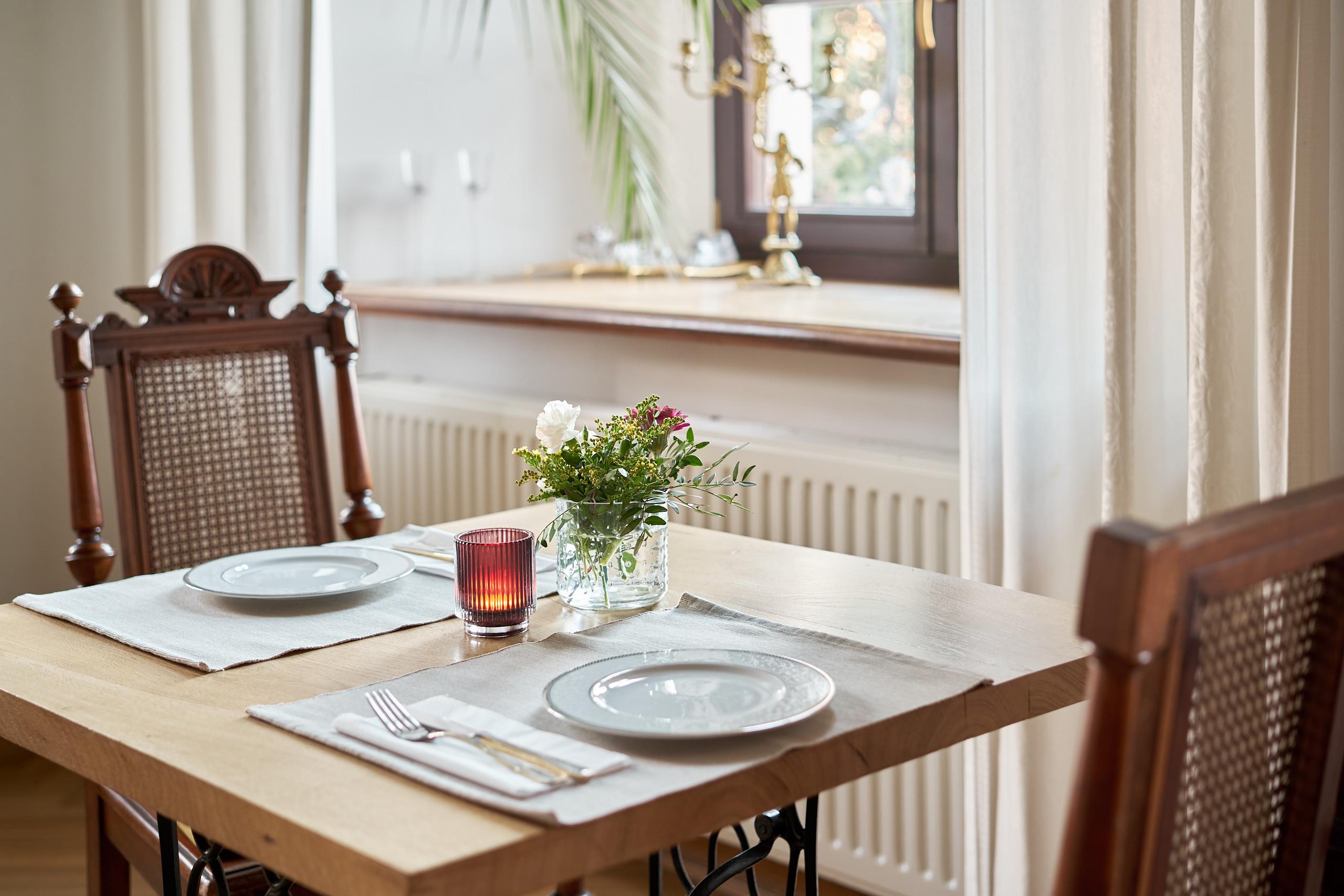 Gedeckter Tisch mit Blumen und Kerze am Fenster
