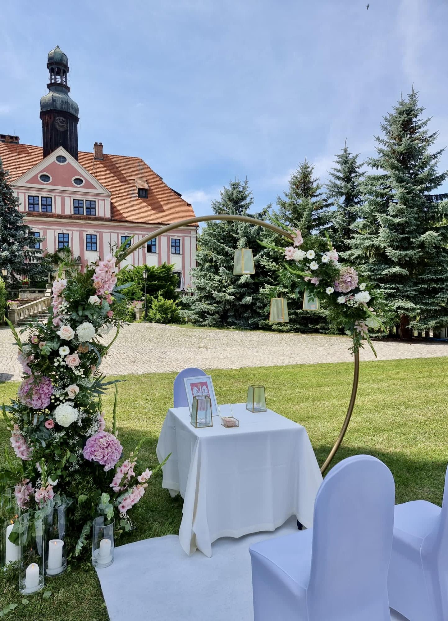 Outdoor ceremony set-up: floral arch, table and chairs before the palace