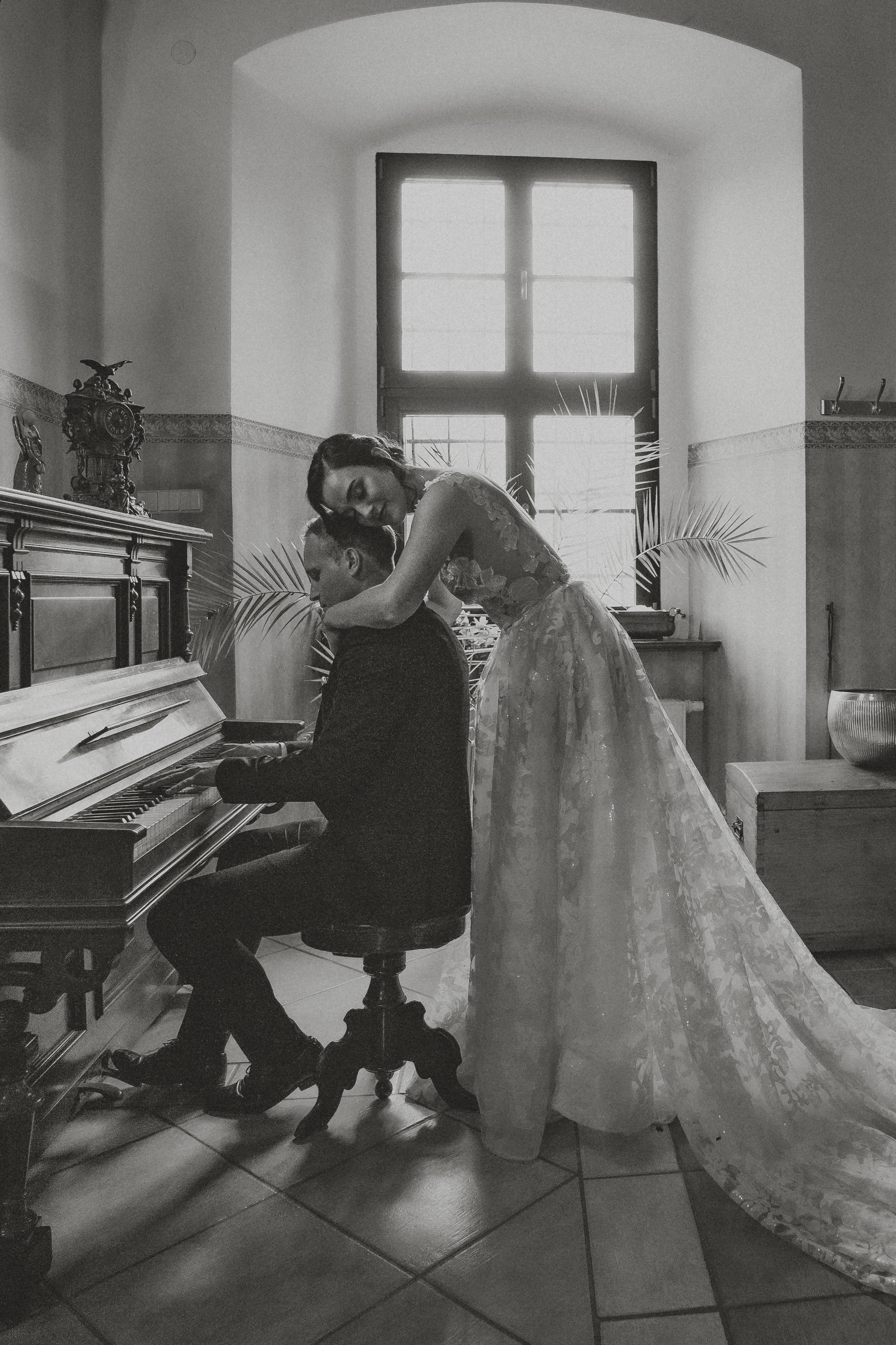 Black-and-white photo of a bride and groom at the piano by a palace window